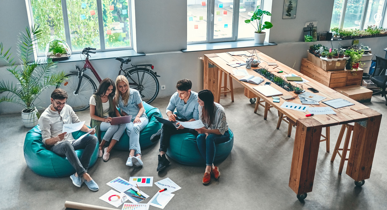 Varias personas reunidas en el suelo con papeles y portátiles compartiendo ideas